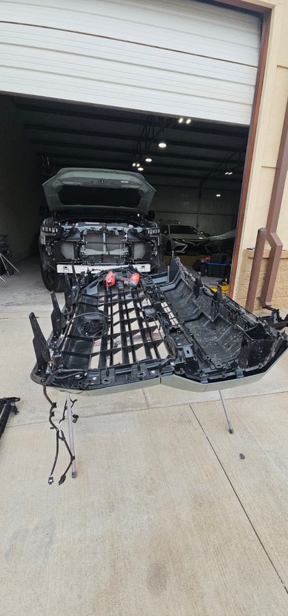 Pickup front bumper assembly removed and set on the ground by the shop door
