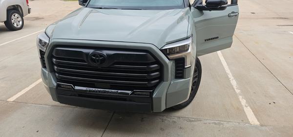 Gray-green pickup front end with grille and bumper reinstalled after repair