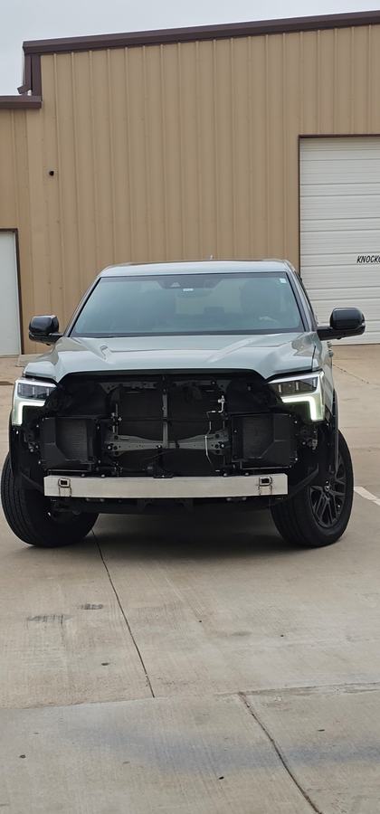 Front view of a gray-green pickup with the bumper and grille removed