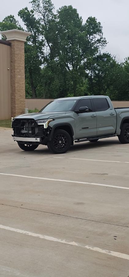 Gray-green pickup with the front bumper and grille removed, parked outside