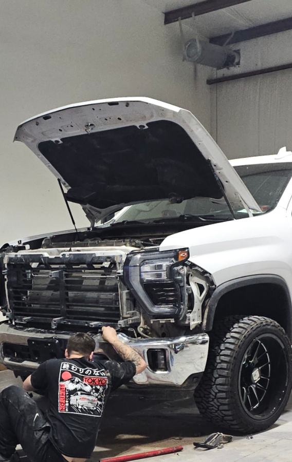 Technician working on the front end of a white heavy-duty pickup with the grille and bumper removed