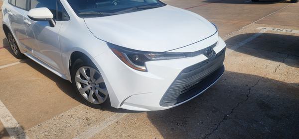 White sedan front three-quarter view after collision repair and refinish, parked outside the shop