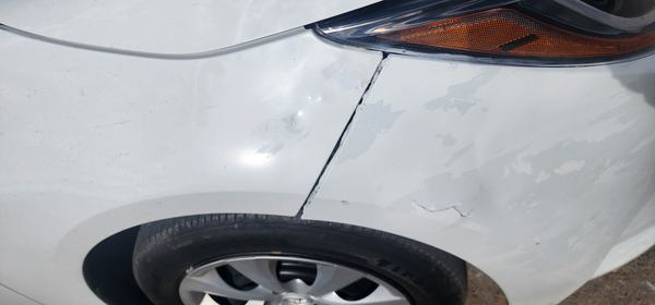 White sedan before repair: dented fender, peeling paint on the bumper and a cracked gap between bumper and fender